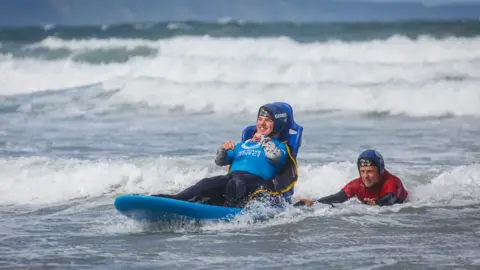 Roy Riley Photography Ian Bennett and George Palmer, a user of the Wave Project, in the sea at Croyde Beach - using adaptive surfing equipment to surf a wave