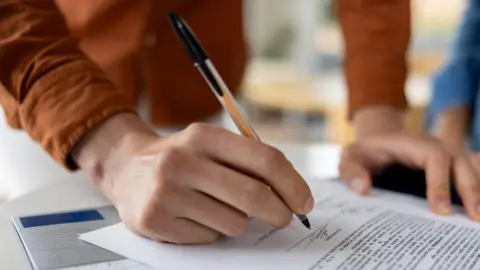 A close-up on a man signing a deed while buying a house.
