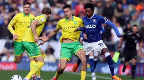 Getty Images Football players push each other on a pitch with busy stands behind them. Three dressed in yellow and green, one dressed in blue.