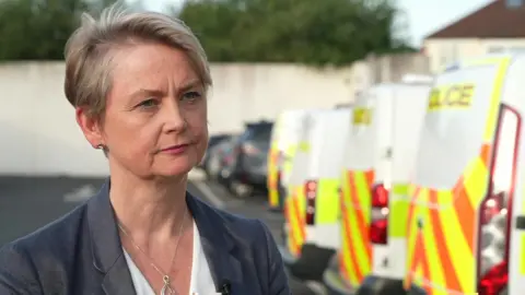 BBC Home Secretary Yvette Cooper stands in front of a line of police vans