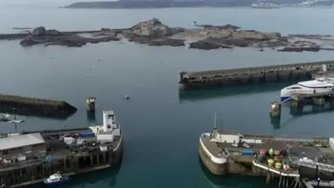 BBC An elevated view of St Helier Harbour showing quaysides and boats. The water is calm.