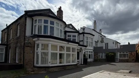 A brick building with bay windows - a large but slightly run down house.