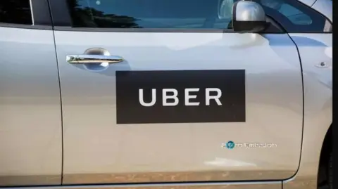 Door of a silver coloured car, with a black sign with "Uber" in white lettering