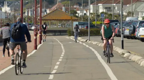 BBC An environmental campaigner says Jersey and Guernsey should be doing more to encourage walking and cycling, alongside electric car use. Image shows people cycling alongside the seafront in St Helier in Jersey