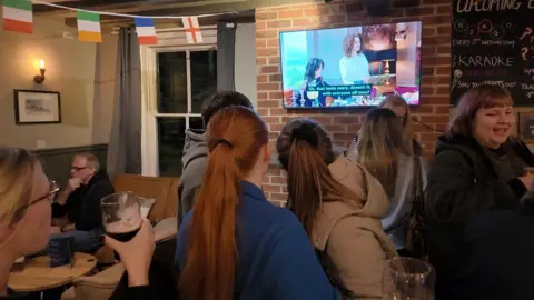 People watching the traitors on the TV in the pub.
