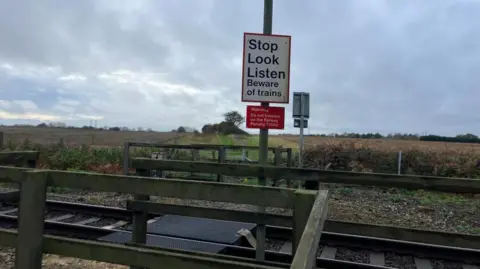 Vikki Irwin/BBC The picture a close up of the railway crossing at Levington Heath which can only be accessed by foot. There is a "Stop Look Listen" sign and the area is surrounded by countryside. 