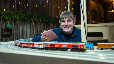 PA Media A man is by a model railway track that includes a mainly red and white model train.
