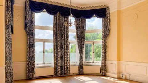 Katrina Woolley A high-ceilinged room in an Edwardian home with ornate curtains 