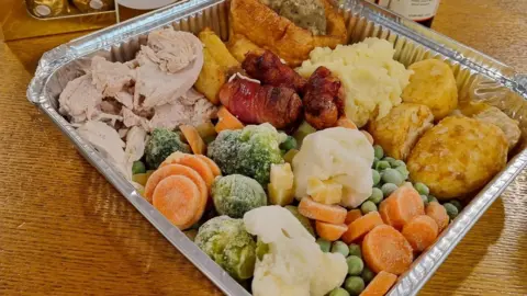 Kath Coogan A full roast dinner inside a takeaway metal tray. There is turkey, carrots, broccoli, cauliflower, pigs in blankets, roast potatoes, Yorkshire pudding, stuffing and roast potatoes