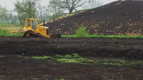 Getty Images A yellow digger in front of a pile of compost in a field of peat