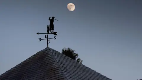 A weather vane with a figure of  a golfer pictured on a roof with the moon in the background