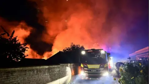 Nicola Hillman A fire engine drives past thick smoke and orange plumes of a fire