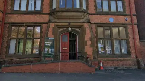 A red brick Gothic building in a picture taken from Google Street View. It has a large red door which is open for visitors.