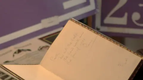 Programmes, posters and tickets from Graham's collection displayed on his kitchen table. A close up image of a book signed by Sir Stanley Rous in pencil. 
