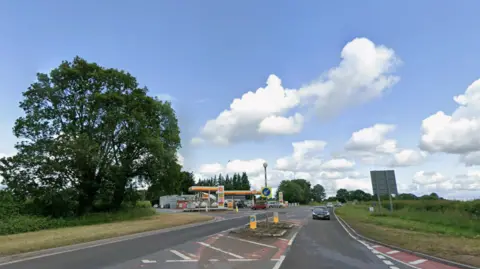 A staggered junction with two entrances. At one junction entrance/exit there is a yellow petrol station. 