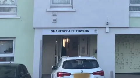 David Spereall/BBC A car parked in front of the communal doorway of a block of flats. The name of the flats sits above the door on a white sign.