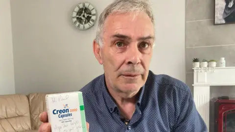 BBC/Piers Hopkirk Paul Elcombe with a pack of the Creon capsules he needs to take