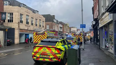 Jewel Miah Baxter Street en Loughborough con vehículos de emergencia estacionados al costado de la carretera, a ambos lados de la cinta policial que se extiende a lo largo de la carretera.