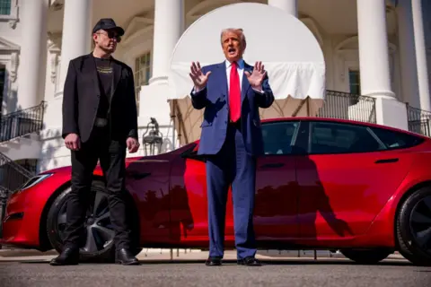 Getty Images Musk and Trump standing in front of a red Tesla