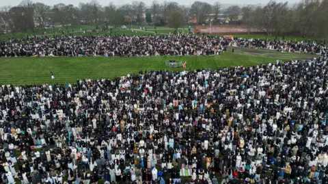A drone view of Muslim men and women praying in a park.