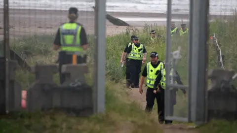Reuters Police in high viz jackets on a beach behind a large fence