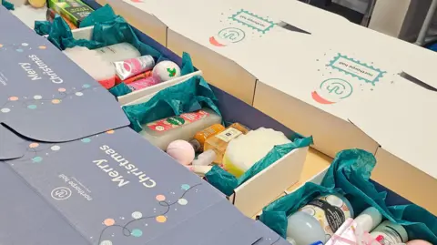 Norhorpe Hall Child and Family Trust A picture of some of the hampers made of cardboard boxes with Merry Christmas and Northorpe Hall printed on them, they contain things like shower gels and bath bombs.