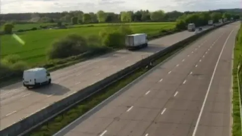 National Highways A road with vehicles queuing on one side. The other side of the road has no vehicles on it.