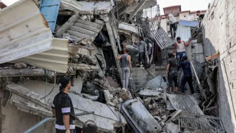 AFP Palestinos tentam resgatar um homem preso sob os restos de um prédio atingido por bombardeios israelenses, no distrito de Saftawi, em Jabalia, no norte da Faixa de Gaza (15 de outubro de 2024)