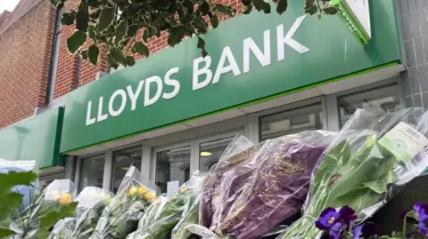 Bunches of flowers laid in front of a Lloyds Bank sign
