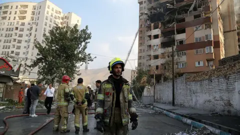 firefighter stands in front of damaged building