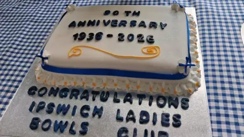 Contributed A celebration cake covered in white icing. Blue icing on it reads: "90th anniversary 1936-2026." Below the cake on a silver tray, more blue icing reads: "Congratulations Ipswich Ladies Bowls Club."