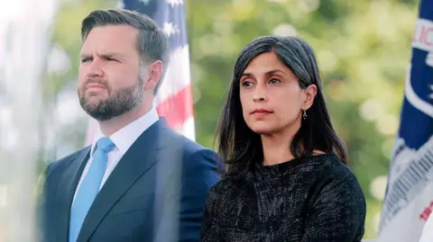 Getty Images Vice-President JD Vance is seen at an event sitting next to his wife, Second Lady Usha Vance. She is wearing a dark-coloured dress and he is wearing a suit with a light blue tie. 