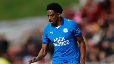 Kyrell Lisbie running on the pitch during a game for Peterborough. He is wearing Peterborough blue kit