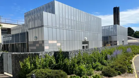 L'unité de soins intensifs de Guernesey vue de l'extérieur. Il s'agit d'un bâtiment gris aux bords rectangulaires nets, adossé à l'hôpital Princess Elizabeth.