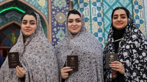 Women hold up their documents after voting in Iran