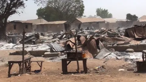 Charred and burned market scene. Destroyed corrugated iron and piles of ash can be seen. 