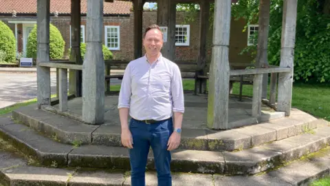 Kate Moser Andon/BBC Chris Carter-Chapman standing in front of a bandstand