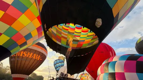 A colourful balloon is inflating as it prepared to take off. Fire can be seen inside the envelope.