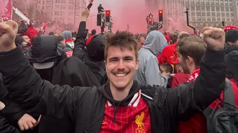 Ross Welsh Ross Welsh, who has short hair and a thin mustache, with a black hood jacket and a FC shirt from the Liverpool and is holding his closed fists in the premier -victory parade of the Premier League. You can see the red smoke behind him