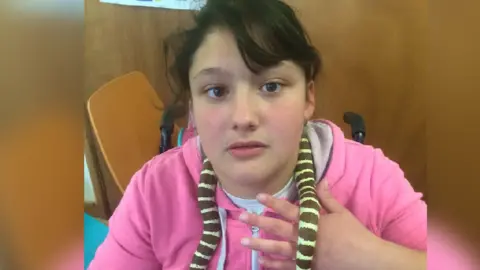 PA Kaylea Titford wearing a pink hoodie, looking into camera with a snake around her neck