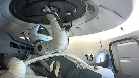 A member of the SpaceX Polaris Dawn crew prepares to open the hatch before a spacewalk