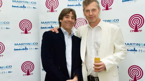 Lee Bolton Photography Comedian Mark Steel, a man in a black suit and light coloured shirt, with Neill Roy, right, wearing a white/cream coloured suit