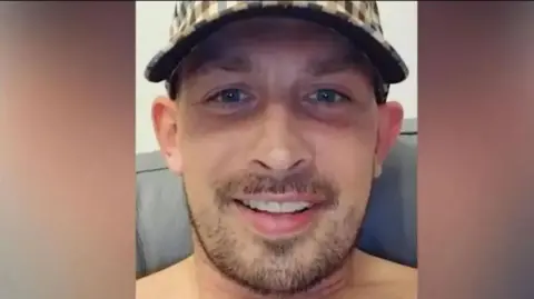 Family photo Lee Crewe is taking a selfie and his bare shoulders are visible. He has light brown stubble and is wearing a check-print baseball cap 