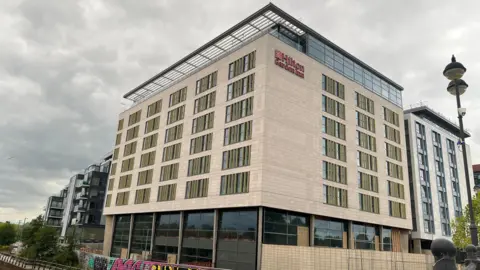 BBC Large hotel with Hilton branding next to river in Peterborough 