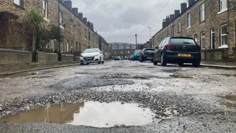A huge pothole with brown rainwater in it on a terraced street