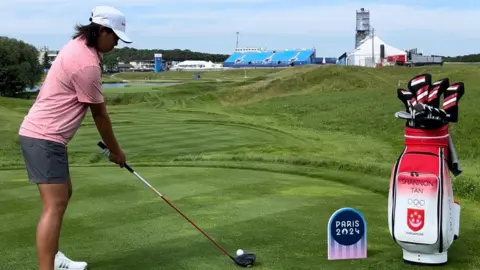 Robin Ellis Shannon Tan preparing for her first round at Le Golf National, she is on the golf course wearing grey shorts and a pink t-shirt, as well as white cap. She is about to hit a golf ball