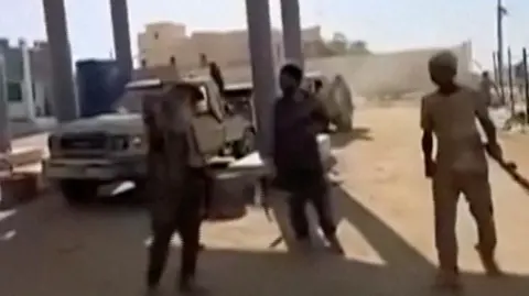 Reuters Three people with guns are pictured at a petrol station and a car is visible in the background