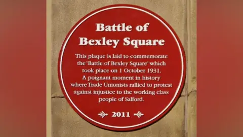 David Dixon/Geograph A red plaque on a brown stone background, reads in white writing: Battle of Bexley Square. This plaque is laid to commemorate the ' Battle of Bexley Square' which took place on 1 October 1931. A poignant moment in history where Trade Unionists rallied to protest against injustice to the working class people of Salford. 2011