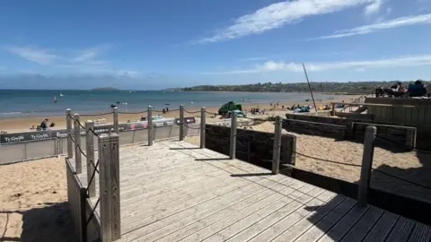 The view from the beach hut's wooden decking showing a long stretch of sand and sea on a sunny day.