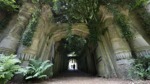 Getty Images A wide shot of the overgrown Egyptian Avenue at Highgate Cemetery, with a silhouetted figure standing at the end of the stone-arched, ivy-covered tunnel.